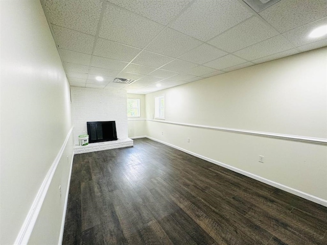 basement featuring a brick fireplace, dark hardwood / wood-style flooring, and a paneled ceiling