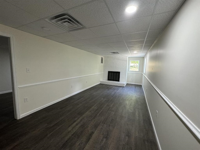 unfurnished living room with a fireplace, a drop ceiling, and dark wood-type flooring