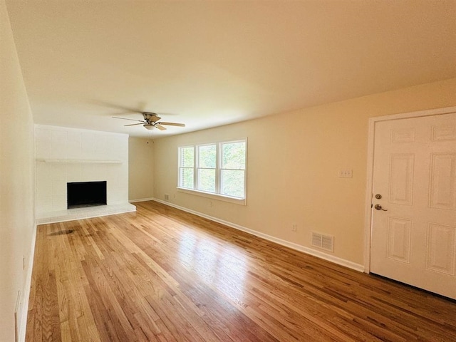 unfurnished living room featuring ceiling fan, light wood-type flooring, and a brick fireplace