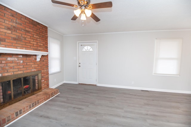 unfurnished living room with ceiling fan, a brick fireplace, hardwood / wood-style floors, crown molding, and a textured ceiling