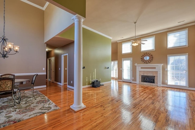 living room with crown molding, a fireplace, a high ceiling, and ornate columns