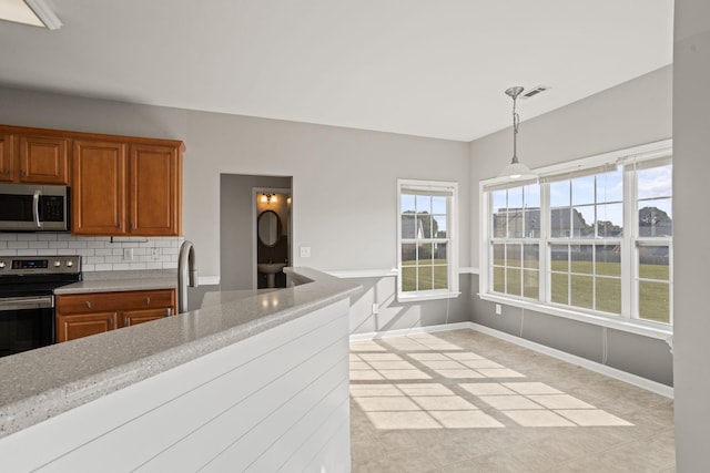 kitchen with light stone countertops, pendant lighting, stainless steel appliances, decorative backsplash, and light tile patterned floors