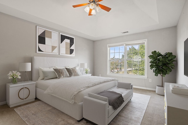 bedroom with ceiling fan, light colored carpet, and a raised ceiling