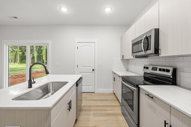 kitchen featuring backsplash, light hardwood / wood-style floors, a center island with sink, sink, and appliances with stainless steel finishes