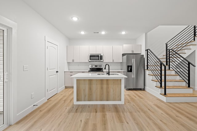 kitchen with backsplash, sink, a kitchen island with sink, appliances with stainless steel finishes, and white cabinets