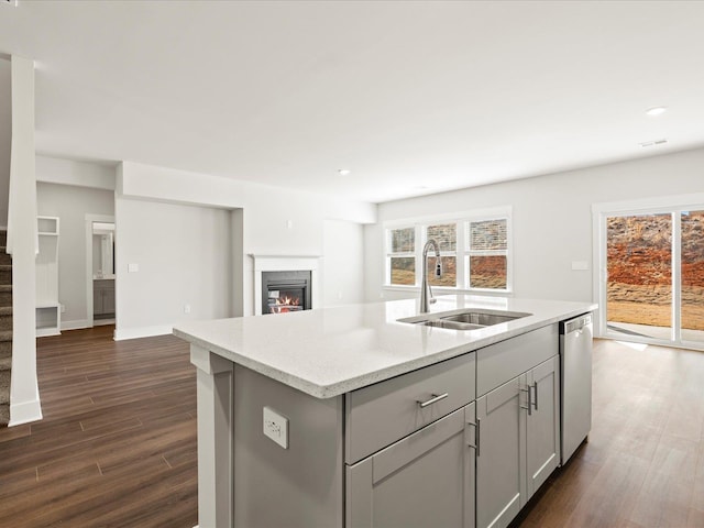 kitchen with an island with sink, dishwasher, dark wood-type flooring, and a sink