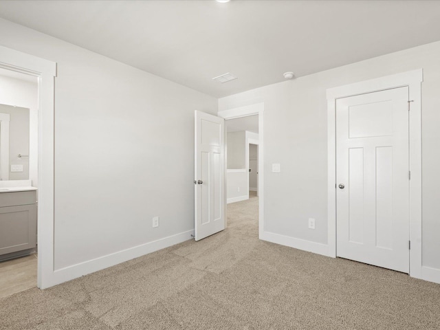 unfurnished bedroom with baseboards, ensuite bathroom, and light colored carpet