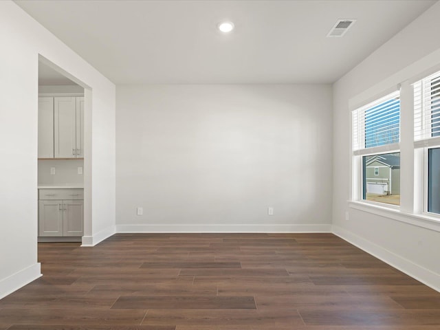 unfurnished room with baseboards, visible vents, dark wood-type flooring, and recessed lighting