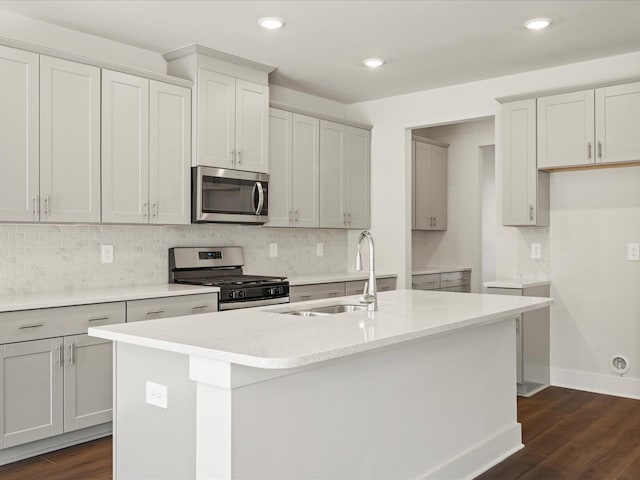 kitchen with a center island with sink, decorative backsplash, dark wood-type flooring, stainless steel appliances, and a sink