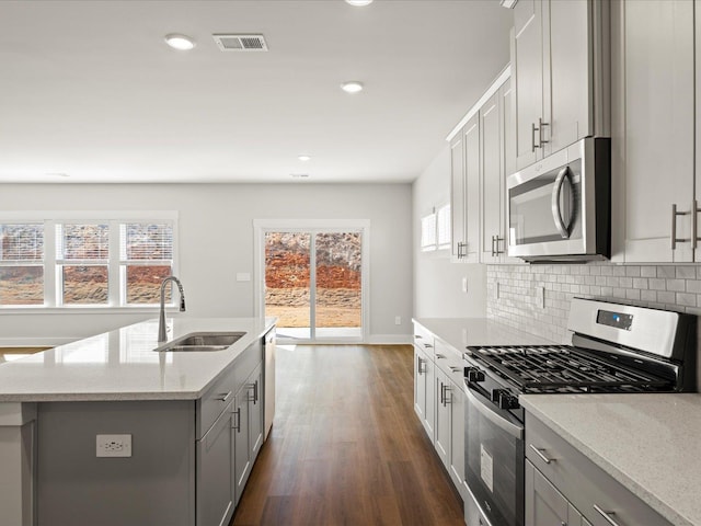 kitchen featuring gray cabinetry, dark wood-style flooring, a sink, appliances with stainless steel finishes, and backsplash