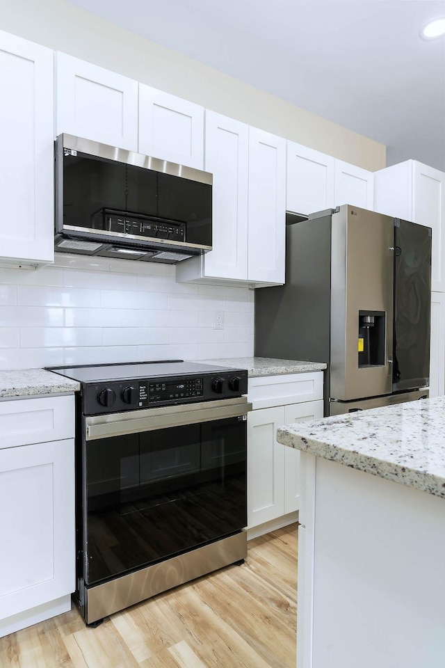 kitchen with light wood-type flooring, stainless steel appliances, white cabinets, and light stone countertops