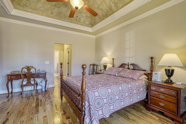 bedroom with ceiling fan, light hardwood / wood-style floors, a tray ceiling, and crown molding