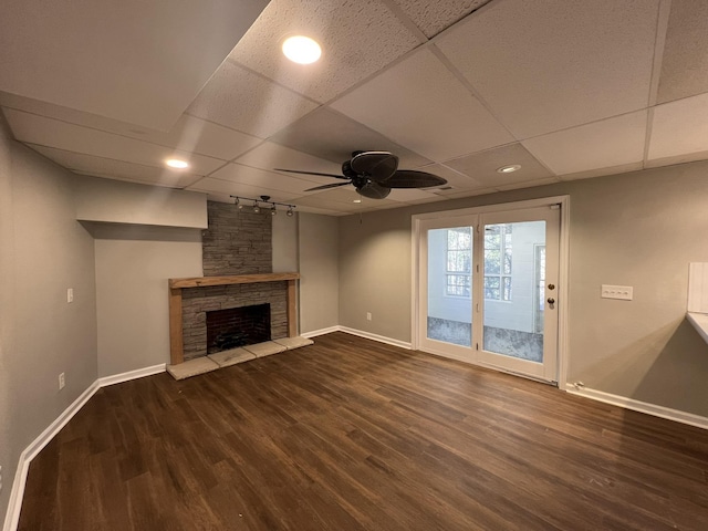 unfurnished living room with ceiling fan, dark wood-type flooring, a fireplace, and a drop ceiling