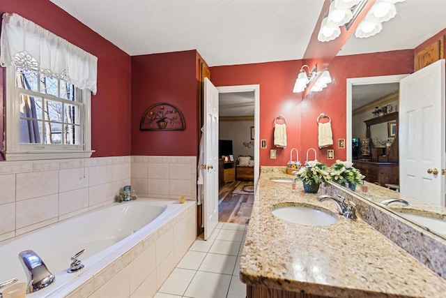 bathroom featuring tile patterned flooring, vanity, tiled bath, and a textured ceiling