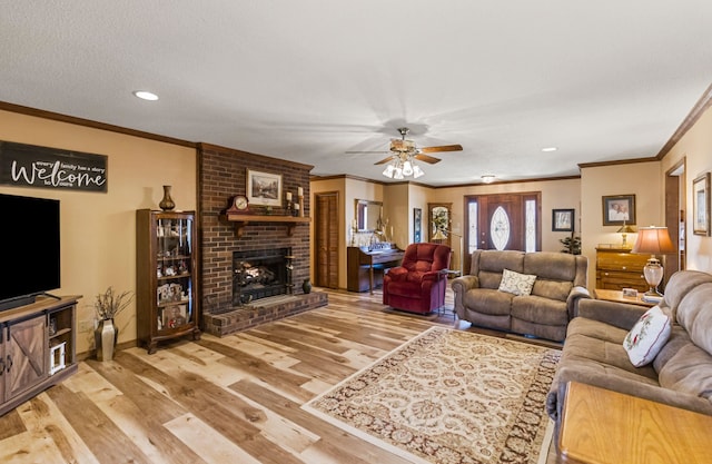 living room with hardwood / wood-style flooring, ceiling fan, ornamental molding, and a fireplace