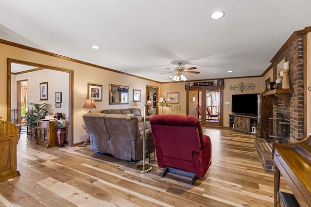 living room featuring a brick fireplace, a textured ceiling, ceiling fan, and light hardwood / wood-style flooring