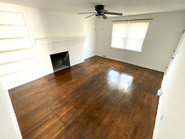 unfurnished living room featuring a brick fireplace, dark wood-type flooring, and ceiling fan