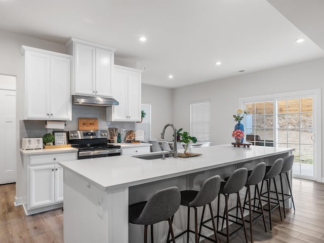 kitchen with stainless steel electric range oven, a center island with sink, sink, and white cabinetry