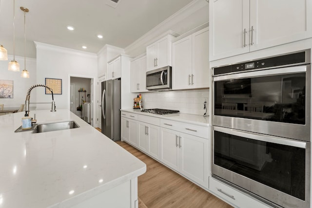 kitchen with hanging light fixtures, appliances with stainless steel finishes, sink, white cabinets, and decorative backsplash