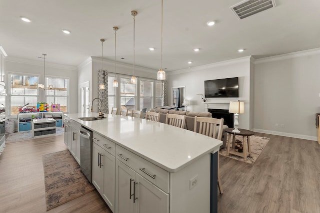 kitchen with sink, pendant lighting, stainless steel dishwasher, and an island with sink