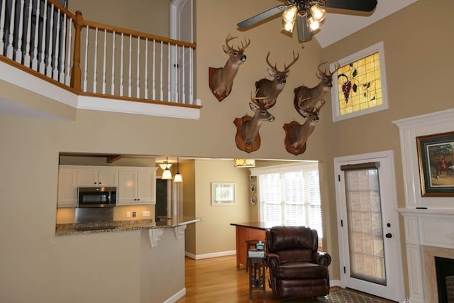 living room with ceiling fan, a towering ceiling, and light wood-type flooring