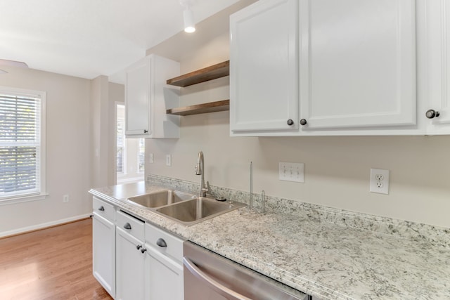 kitchen with light stone countertops, white cabinetry, stainless steel dishwasher, sink, and light wood-type flooring