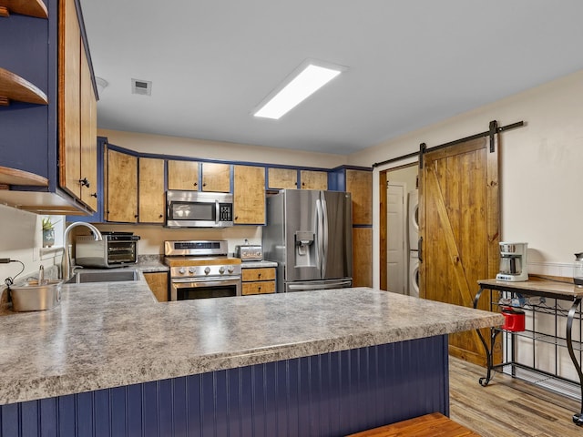 kitchen with stacked washer and dryer, light hardwood / wood-style flooring, appliances with stainless steel finishes, kitchen peninsula, and a barn door