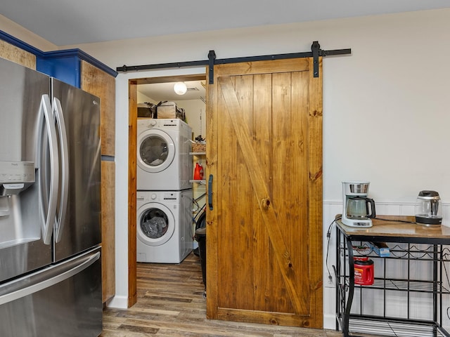 laundry room featuring stacked washer / drying machine, a barn door, and hardwood / wood-style floors