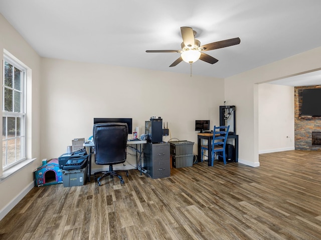 home office with dark hardwood / wood-style flooring, a stone fireplace, and ceiling fan