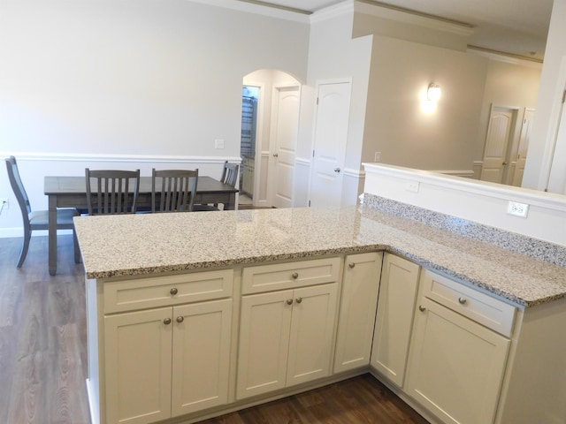 kitchen with cream cabinets, dark hardwood / wood-style floors, kitchen peninsula, and light stone countertops