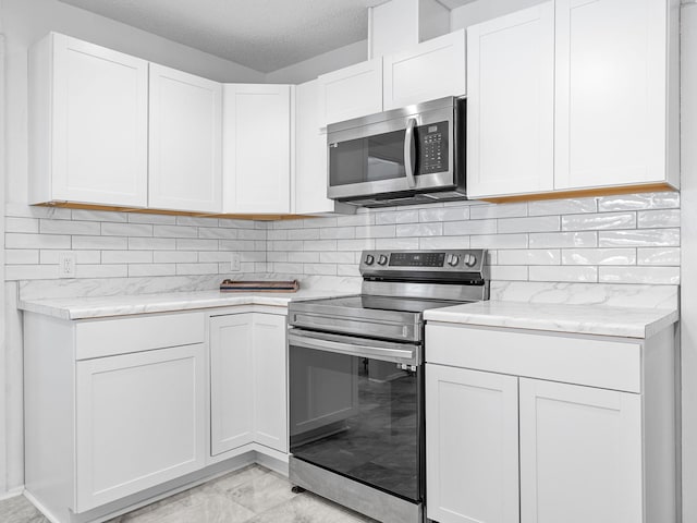 kitchen with appliances with stainless steel finishes, tasteful backsplash, white cabinetry, light stone countertops, and a textured ceiling