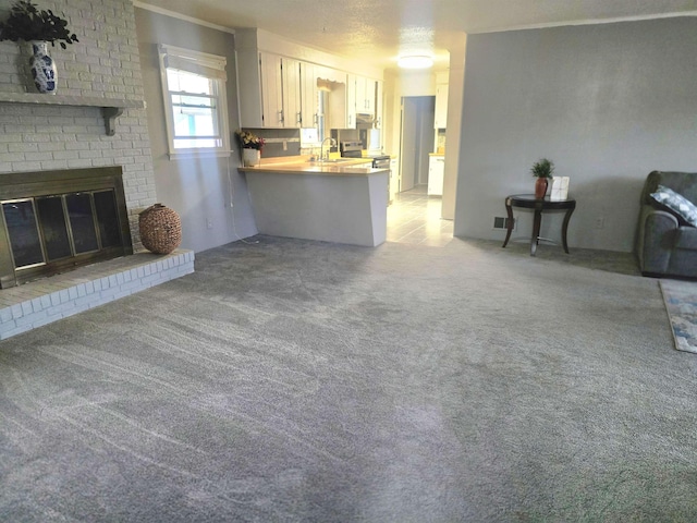 unfurnished living room featuring sink, a brick fireplace, and light colored carpet