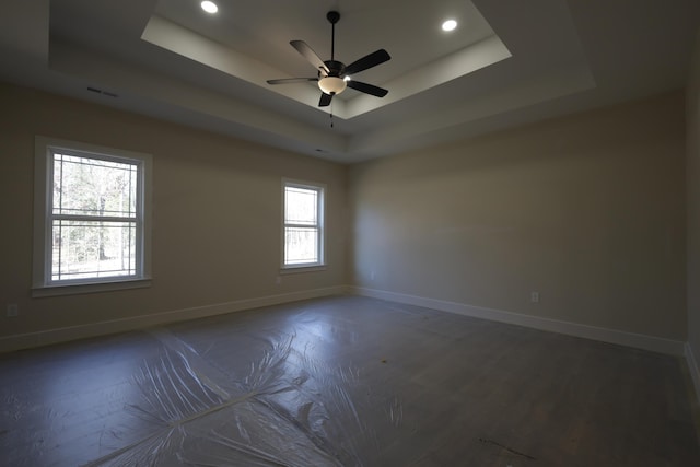 empty room with plenty of natural light, ceiling fan, and a raised ceiling