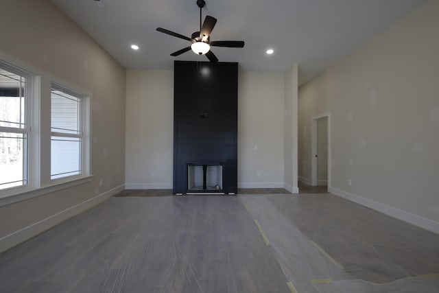 unfurnished living room featuring wood-type flooring, ceiling fan, and a large fireplace