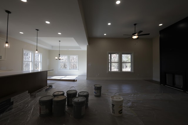 living room with ceiling fan with notable chandelier and a tray ceiling