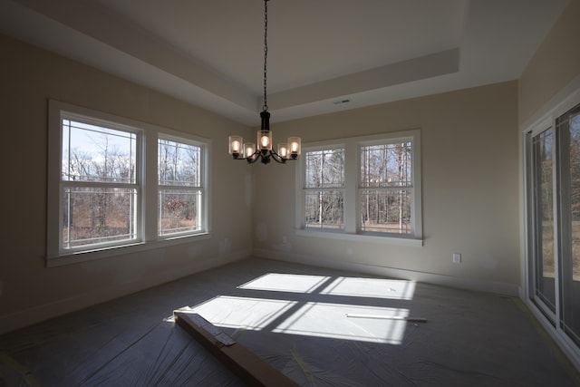 unfurnished dining area featuring an inviting chandelier, a wealth of natural light, and a raised ceiling