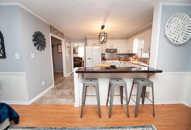 kitchen with kitchen peninsula, white cabinets, white fridge with ice dispenser, a breakfast bar, and range