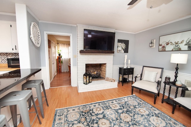 living room featuring a fireplace, light hardwood / wood-style flooring, ceiling fan, and ornamental molding