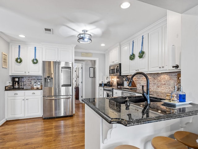 kitchen with white cabinetry, stainless steel appliances, kitchen peninsula, and dark stone counters