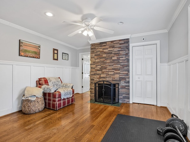 living room featuring hardwood / wood-style flooring, ceiling fan, ornamental molding, and a fireplace