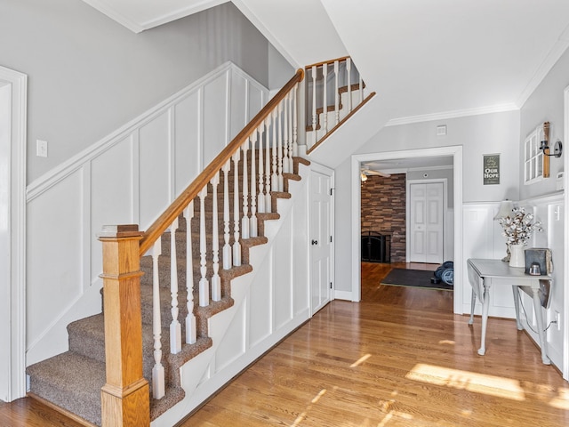 stairway featuring crown molding, a stone fireplace, and hardwood / wood-style floors