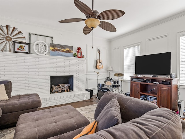 living room with a brick fireplace, crown molding, wood-type flooring, and ceiling fan