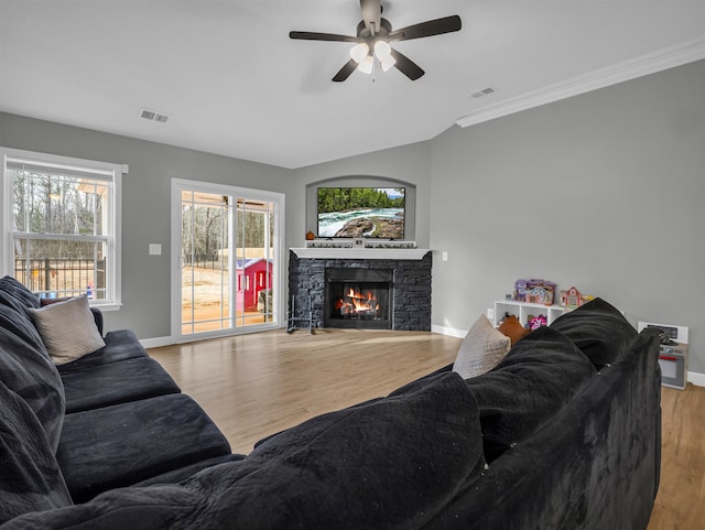 living room featuring ceiling fan, plenty of natural light, a stone fireplace, and light hardwood / wood-style flooring