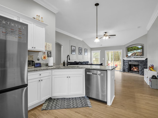 kitchen featuring appliances with stainless steel finishes, a stone fireplace, stone countertops, white cabinetry, and sink