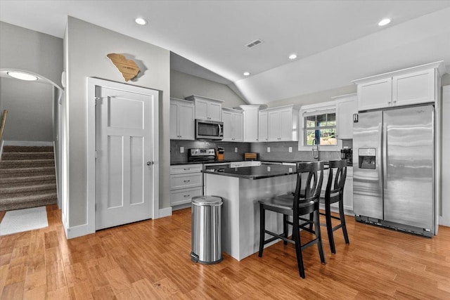 kitchen with appliances with stainless steel finishes, lofted ceiling, white cabinets, a kitchen breakfast bar, and decorative backsplash