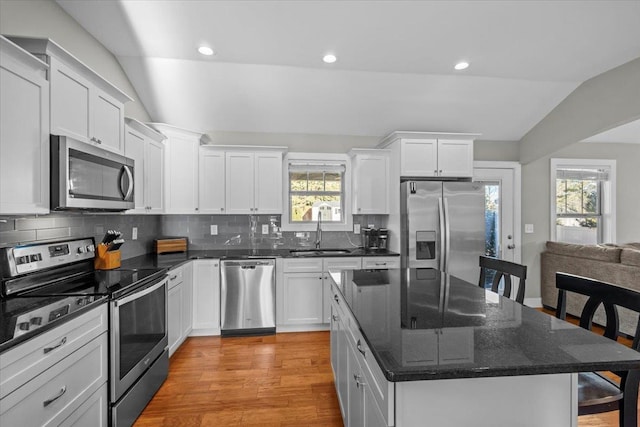 kitchen featuring lofted ceiling, sink, stainless steel appliances, white cabinets, and a kitchen island