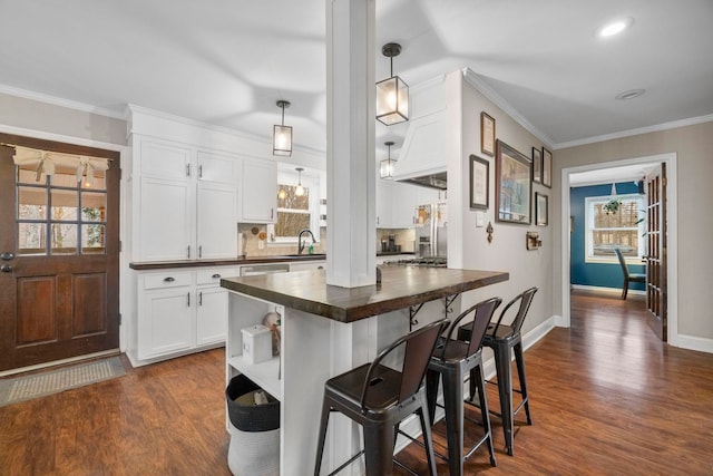 kitchen featuring sink, a kitchen breakfast bar, white cabinets, pendant lighting, and backsplash