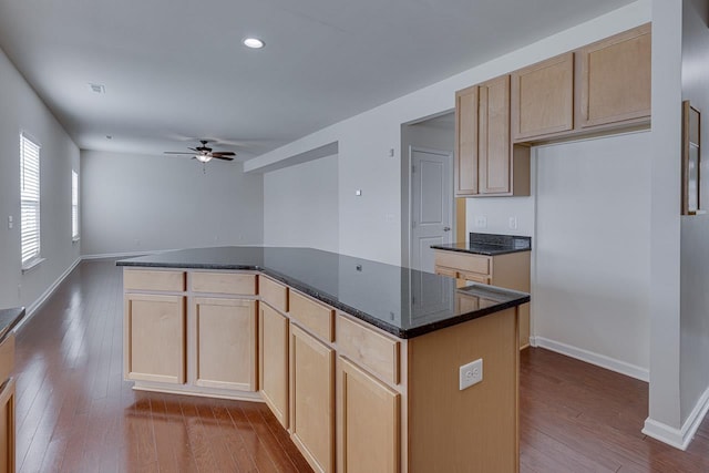 kitchen featuring ceiling fan, dark stone countertops, wood-type flooring, a kitchen island, and light brown cabinetry