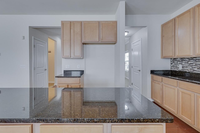 kitchen featuring backsplash, light brown cabinetry, and dark stone countertops