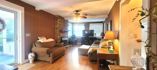 living room featuring a stone fireplace, hardwood / wood-style floors, wooden walls, ceiling fan, and beam ceiling